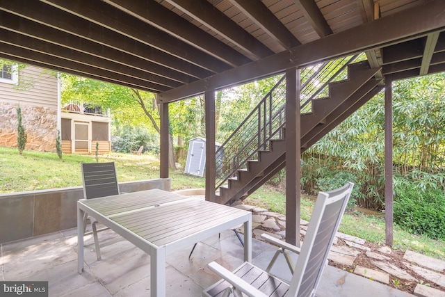 view of patio / terrace with an outbuilding, a shed, outdoor dining space, and stairway