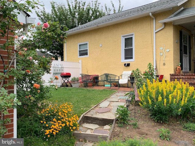 exterior space featuring a yard, roof with shingles, and stucco siding