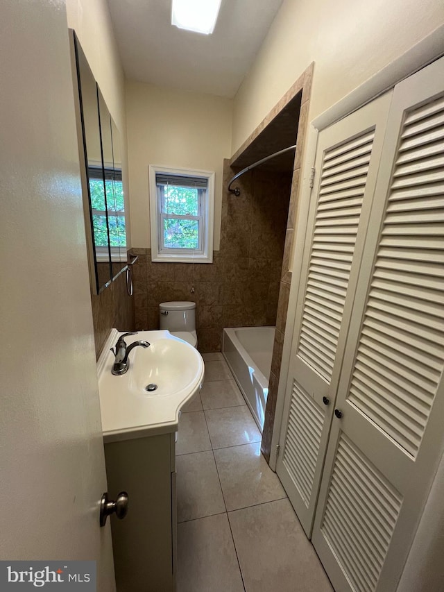 bathroom with tile walls, a closet, toilet, vanity, and tile patterned flooring