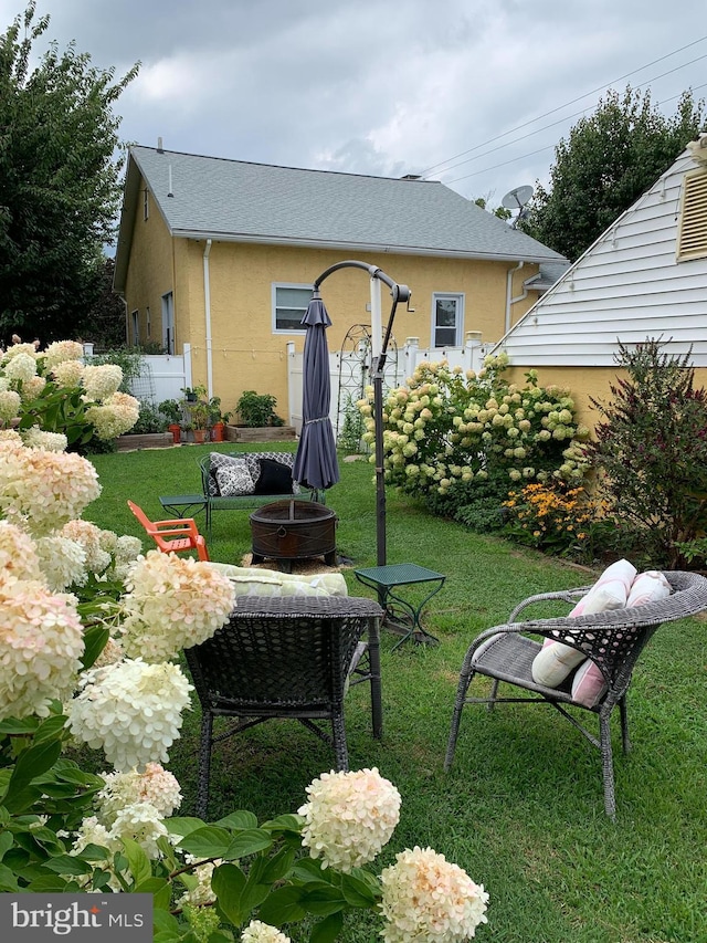 rear view of property featuring an outdoor fire pit, a lawn, fence, and stucco siding