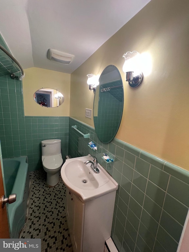 full bath featuring a bathtub, a wainscoted wall, tile walls, toilet, and vanity