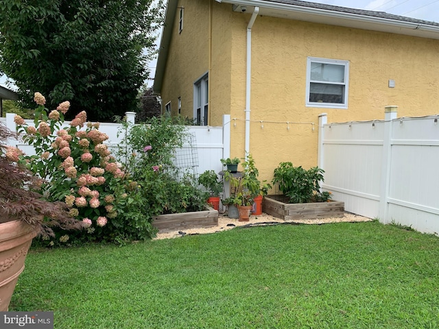 view of side of property featuring a lawn, fence, a vegetable garden, and stucco siding