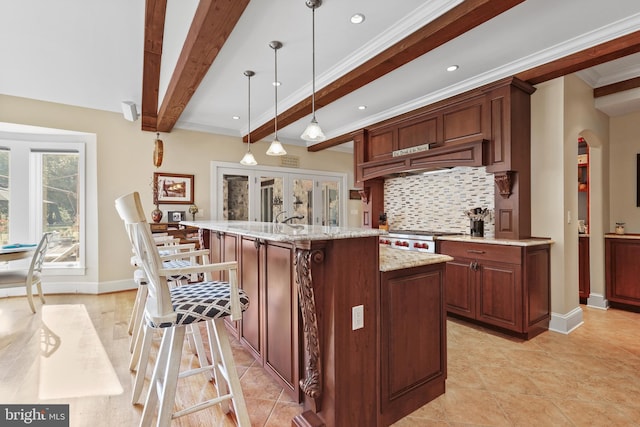 kitchen featuring ornamental molding, tasteful backsplash, decorative light fixtures, light stone counters, and an island with sink