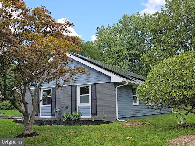 view of front facade featuring solar panels, brick siding, and a front lawn