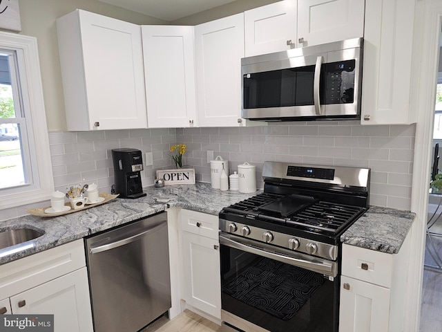 kitchen with white cabinetry, appliances with stainless steel finishes, decorative backsplash, and light stone countertops