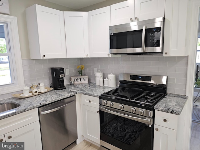 kitchen with appliances with stainless steel finishes, white cabinets, light stone counters, and tasteful backsplash