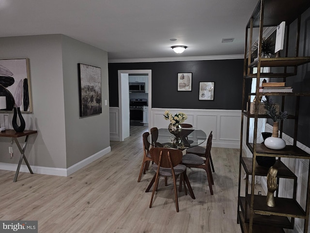 dining room featuring light wood-type flooring, visible vents, a decorative wall, and ornamental molding