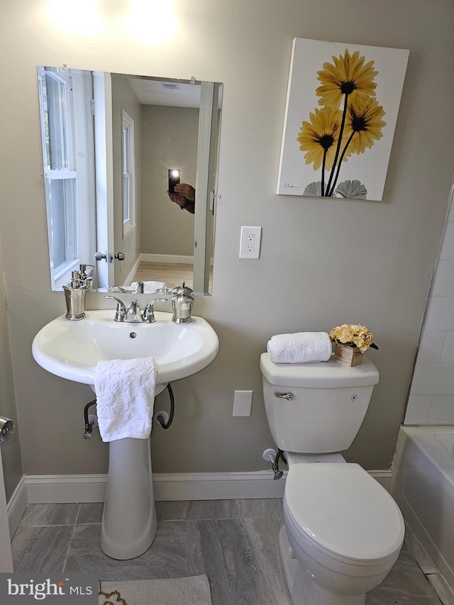 full bathroom with a washtub, baseboards, and toilet