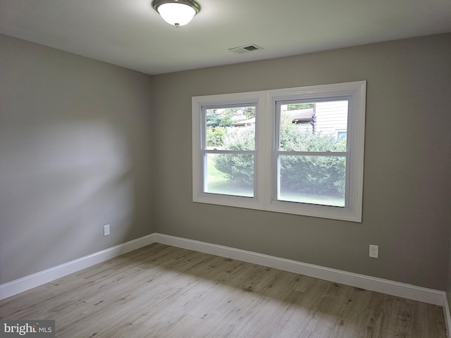 spare room featuring light wood-type flooring, visible vents, and baseboards