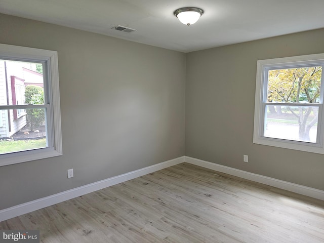 spare room featuring light wood-style floors, a wealth of natural light, visible vents, and baseboards