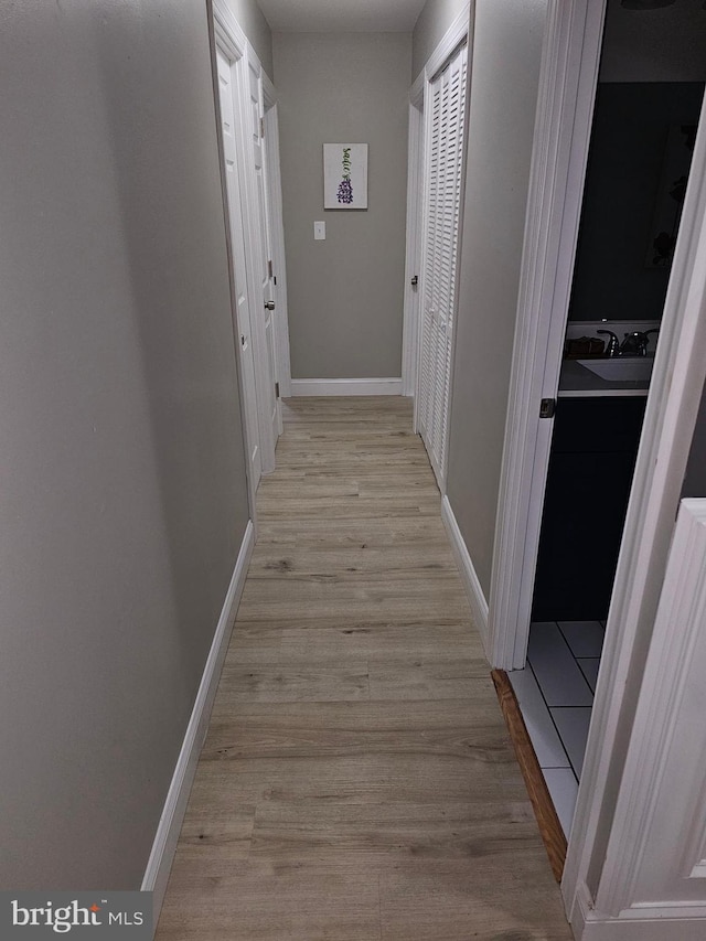 corridor with light wood-type flooring, a sink, and baseboards