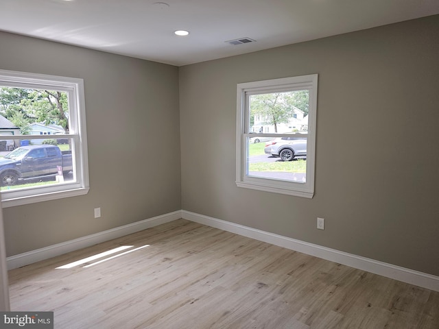 spare room featuring light wood-style floors, plenty of natural light, and visible vents