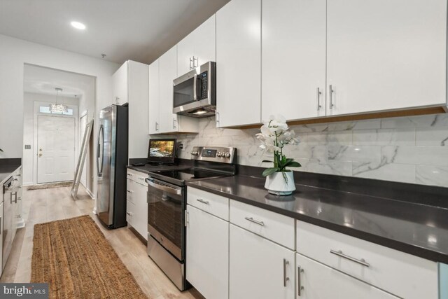 kitchen featuring stainless steel appliances, light wood-type flooring, white cabinetry, and decorative backsplash