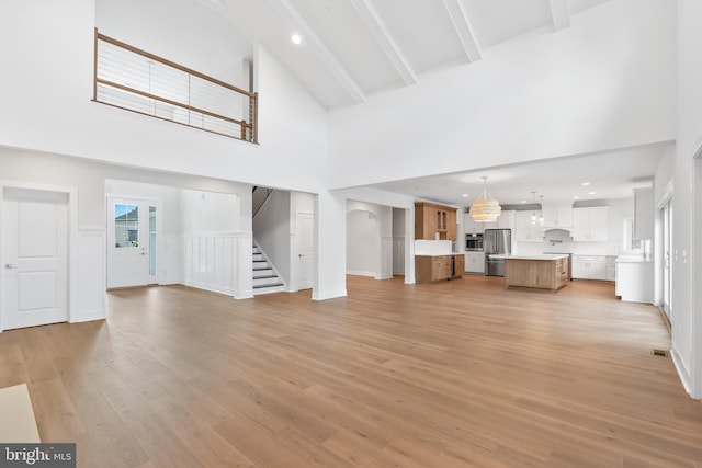 unfurnished living room with beam ceiling, high vaulted ceiling, and light hardwood / wood-style flooring