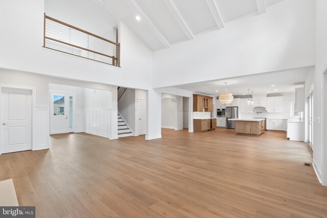 unfurnished living room featuring light wood-style floors, beamed ceiling, stairway, and a towering ceiling