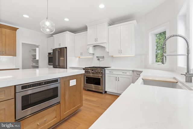 kitchen with light hardwood / wood-style flooring, pendant lighting, white cabinets, appliances with stainless steel finishes, and sink