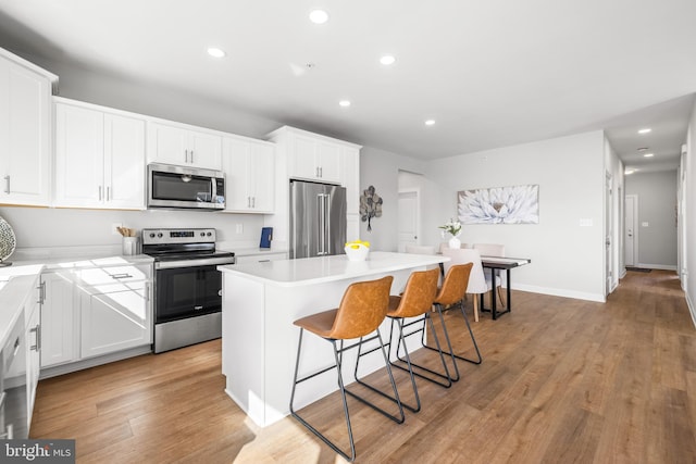 kitchen featuring light wood finished floors, a kitchen island, a breakfast bar area, appliances with stainless steel finishes, and white cabinetry