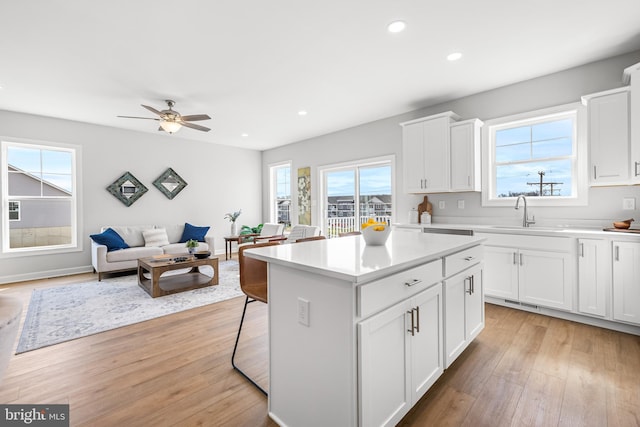 kitchen featuring a kitchen island, light countertops, light wood-style floors, white cabinetry, and a sink