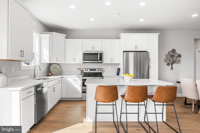 kitchen with light wood finished floors, a sink, appliances with stainless steel finishes, a kitchen breakfast bar, and a center island