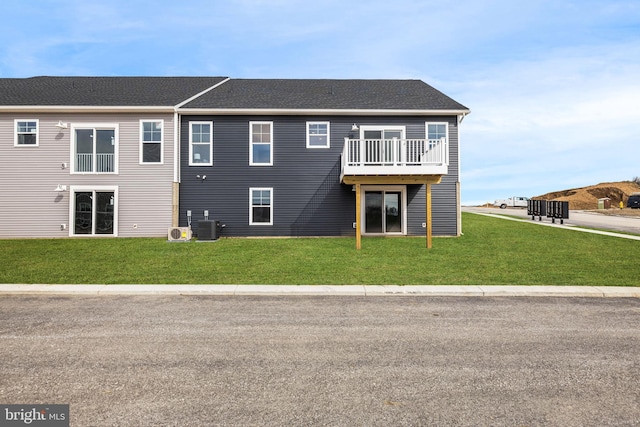 rear view of property featuring a wooden deck, a lawn, cooling unit, and a shingled roof