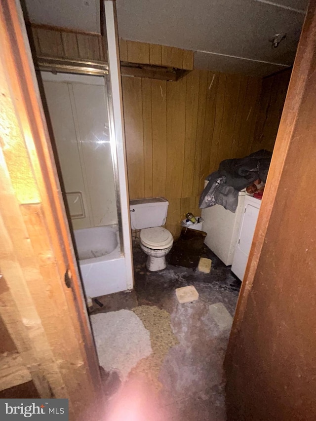 bathroom with washing machine and clothes dryer, shower / bath combination, concrete floors, toilet, and wooden walls