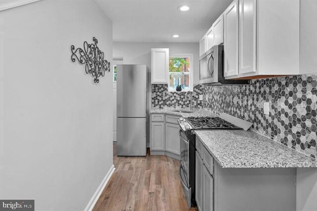 kitchen with decorative backsplash, light hardwood / wood-style floors, light stone counters, stainless steel appliances, and sink