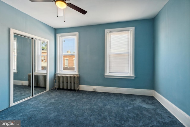 unfurnished room with baseboards, dark carpet, and radiator