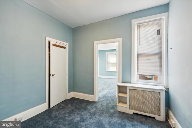 unfurnished bedroom with dark colored carpet, baseboards, and radiator heating unit