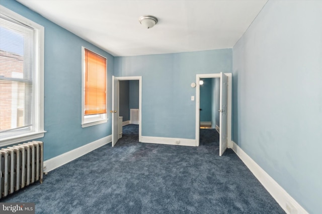 unfurnished bedroom featuring dark colored carpet, radiator heating unit, and baseboards