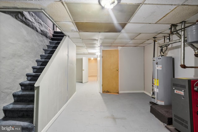 finished below grade area featuring stairs, gas water heater, and a paneled ceiling