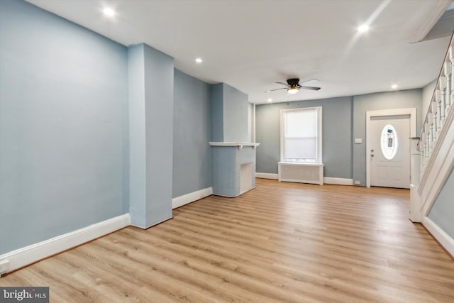 interior space with a ceiling fan, baseboards, stairs, radiator, and light wood finished floors