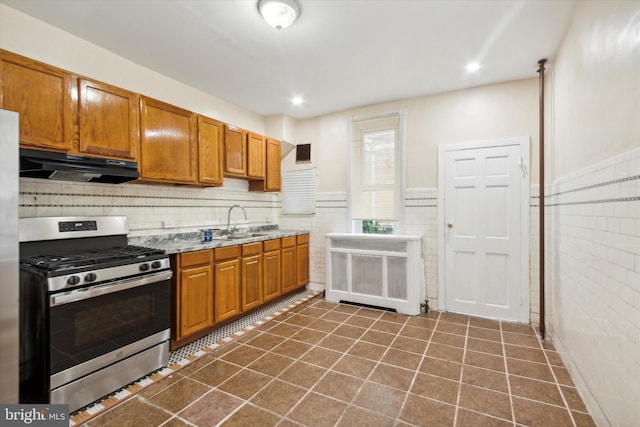 kitchen with under cabinet range hood, dark tile patterned floors, a sink, brown cabinetry, and gas range