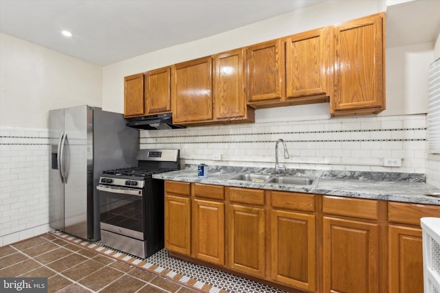 kitchen featuring under cabinet range hood, stainless steel appliances, a sink, light stone countertops, and brown cabinetry