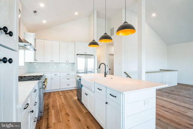 kitchen featuring high quality appliances, white cabinetry, hanging light fixtures, light stone countertops, and wall chimney exhaust hood