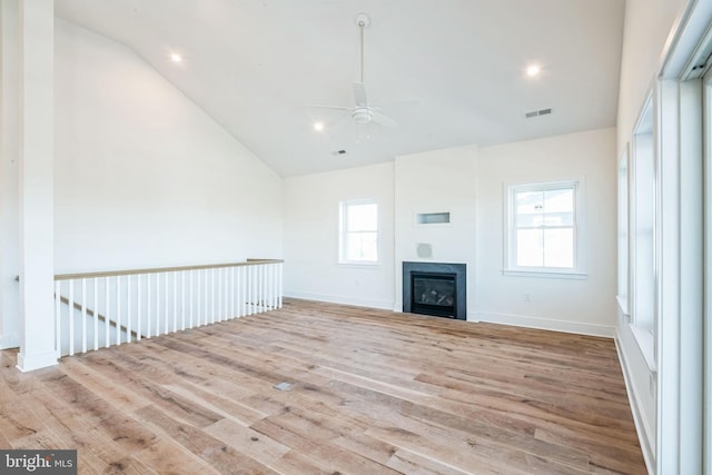 unfurnished living room with visible vents, a ceiling fan, a glass covered fireplace, lofted ceiling, and light wood-style flooring