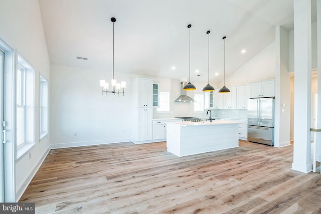 kitchen with a kitchen island with sink, light countertops, high end fridge, and decorative light fixtures