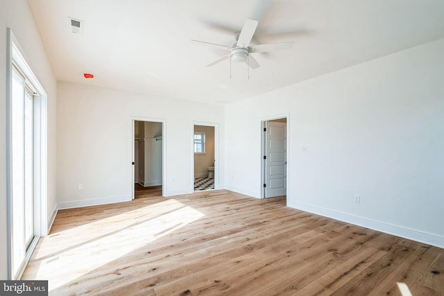 unfurnished bedroom featuring connected bathroom, light wood-style flooring, visible vents, baseboards, and a spacious closet