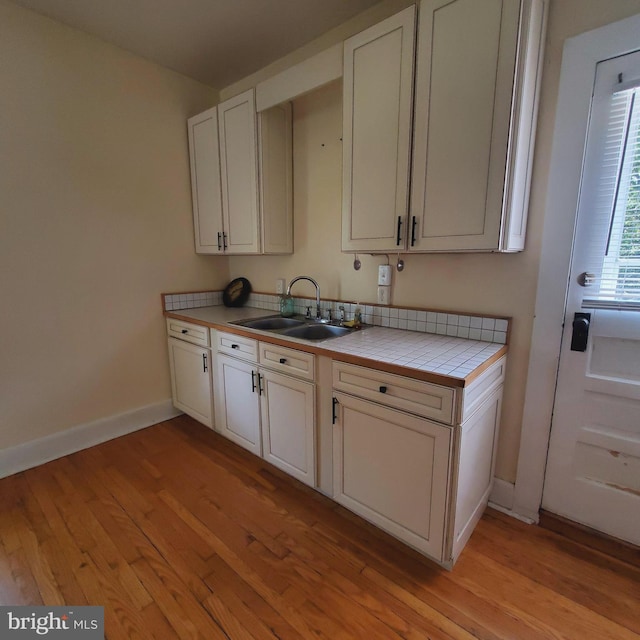 kitchen featuring light wood-style flooring, tile counters, white cabinets, and a sink