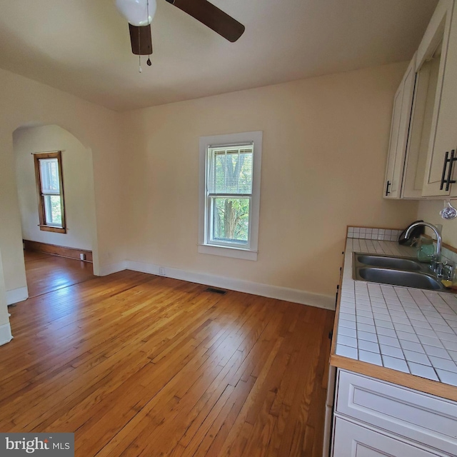 kitchen featuring tile countertops, a healthy amount of sunlight, a sink, and white cabinets