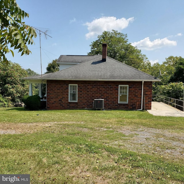 exterior space featuring cooling unit, brick siding, a yard, and a chimney