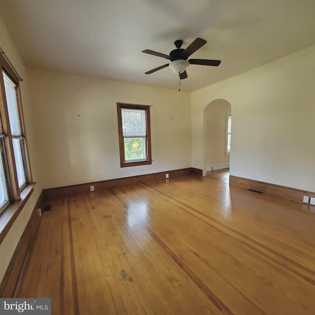 empty room featuring arched walkways, visible vents, light wood-style flooring, ceiling fan, and baseboards