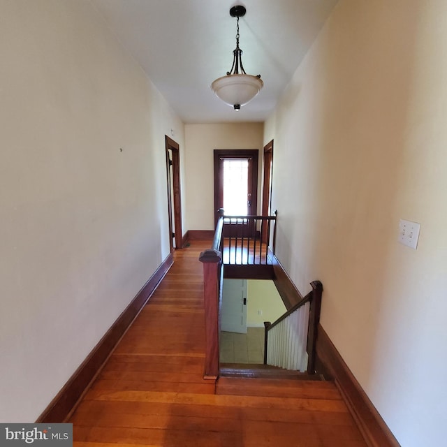 hallway featuring baseboards, dark wood-style flooring, and an upstairs landing