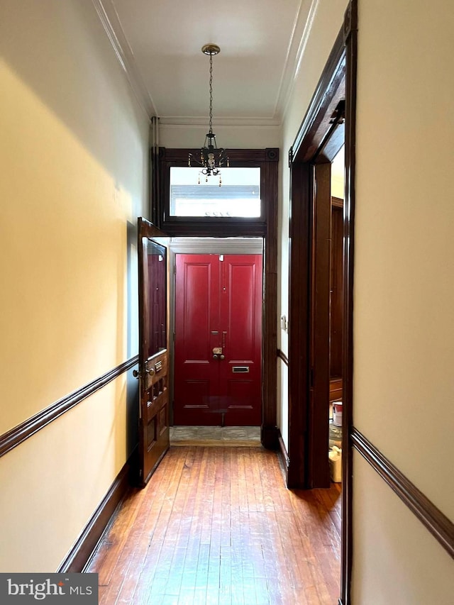 corridor with a chandelier, ornamental molding, light wood-style flooring, and baseboards