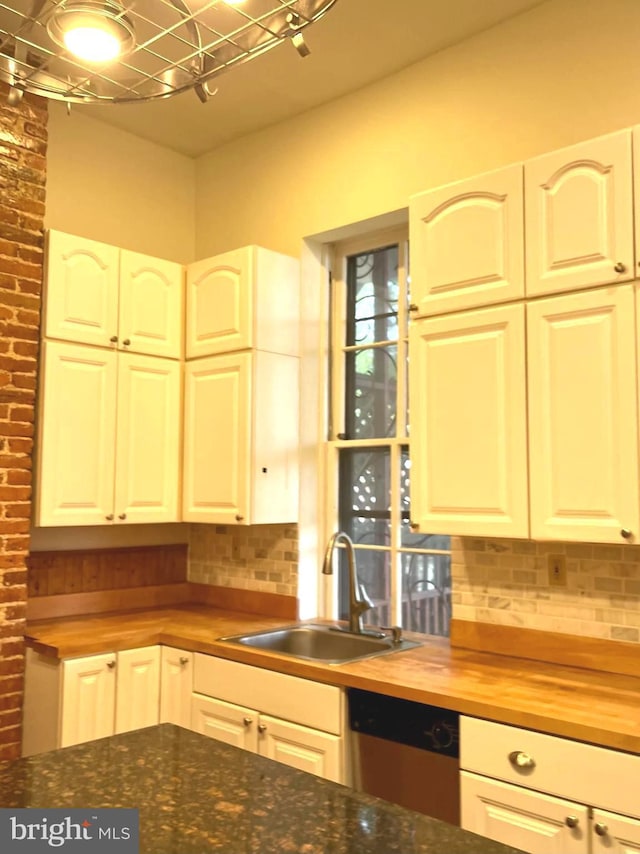 kitchen featuring butcher block countertops, a sink, white cabinetry, stainless steel dishwasher, and decorative backsplash