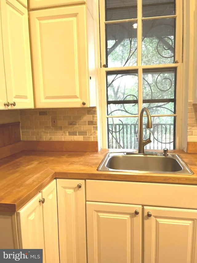 kitchen featuring butcher block countertops, a healthy amount of sunlight, a sink, and decorative backsplash