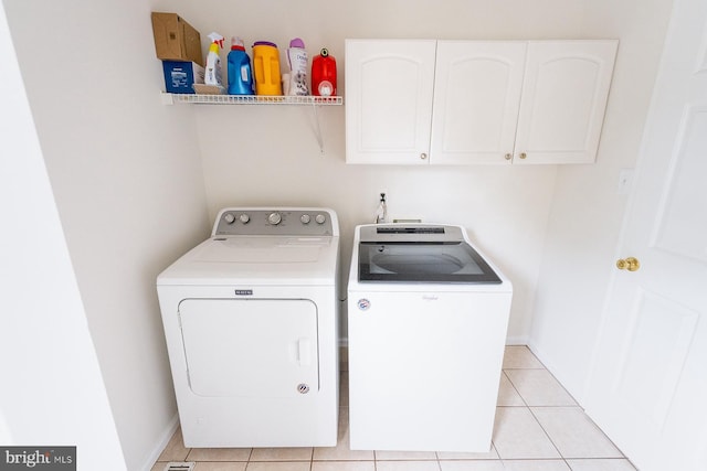 clothes washing area featuring cabinets, light tile patterned floors, and washer and clothes dryer