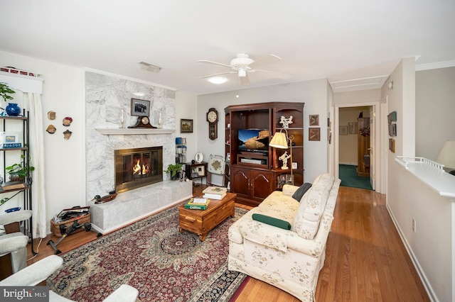 living room with a large fireplace, crown molding, hardwood / wood-style flooring, and ceiling fan