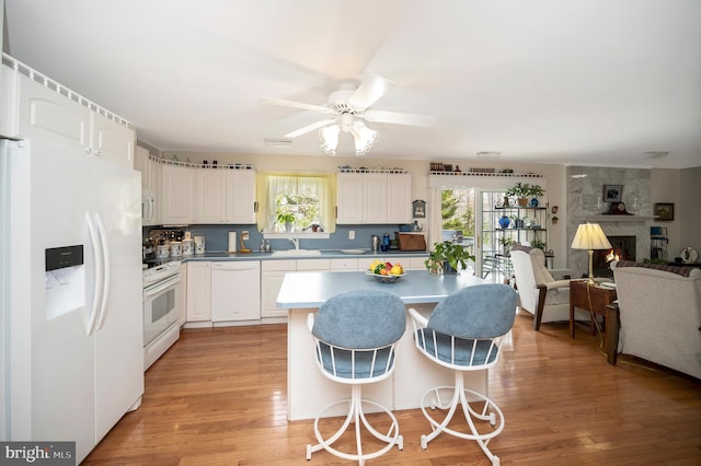 kitchen with light hardwood / wood-style floors, ceiling fan, white appliances, a large fireplace, and white cabinets