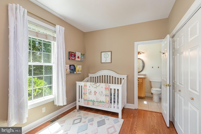 bedroom featuring multiple windows, light wood-type flooring, ensuite bath, and a crib