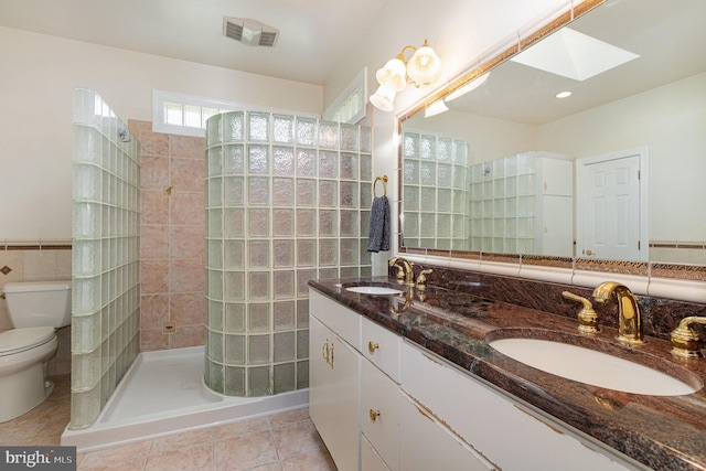 bathroom featuring a skylight, tile patterned floors, a tile shower, vanity, and toilet